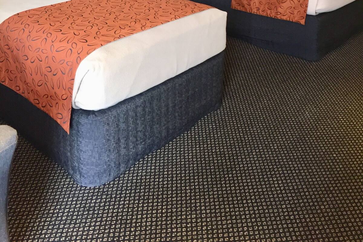 A hotel room with two beds, each with a patterned bedspread, a nightstand with a lamp, and a painting on the wall.