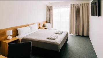 Quarto de hotel com uma cama grande, duas mesas de cabeceira com luminárias, uma TV de tela plana na parede e vista para o exterior pela janela.