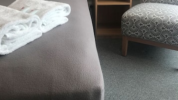Una habitación de hotel con cama, mesita de noche con lámpara y un sillón con estampado.