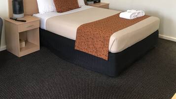 Habitación de hotel con cama, mesita de noche, lámpara, unidad de aire acondicionado y un cuadro en la pared.