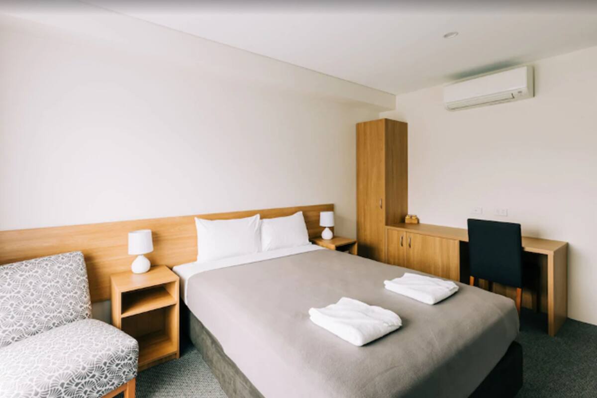 A hotel room with a bed, a desk, a chair, and a wardrobe.