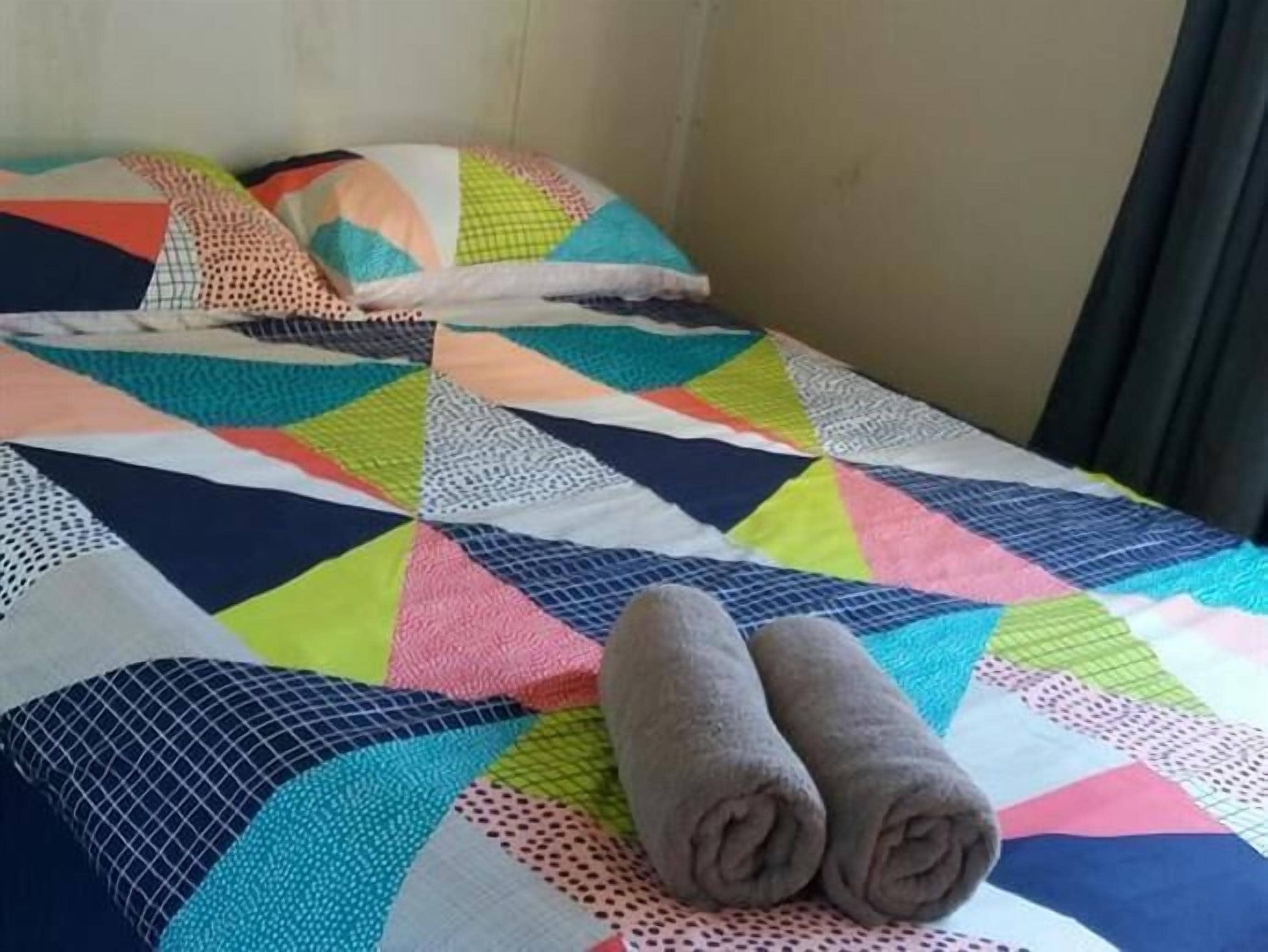 A bed with a colorful patchwork quilt and two rolled towels on it.