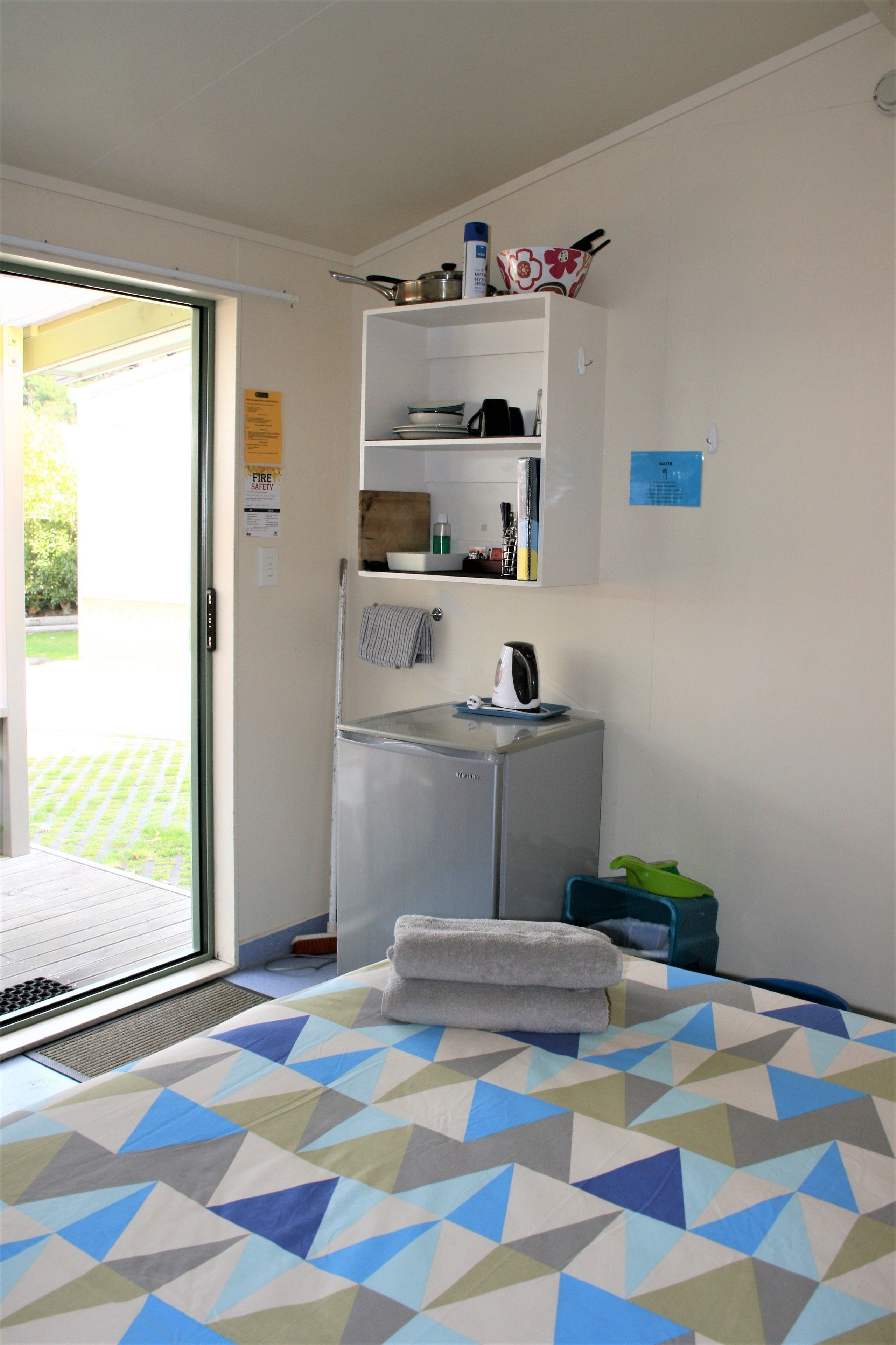 A hotel room with a bed, a small kitchenette, a window, and a door leading to a balcony.