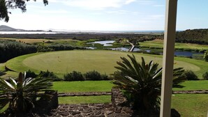 A golf course with a pond, palm trees, and a distant mountain range. - Whatuwhiwhi TOP 10 Holiday Park (Karkari Peninsula)