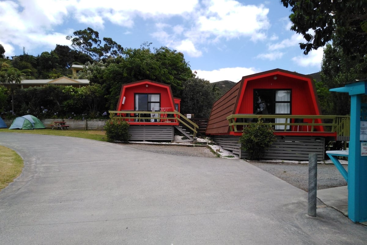 Deux petites cabanes rouges, dotées de rampes en bois, et un chemin en béton menant à ces cabanes.