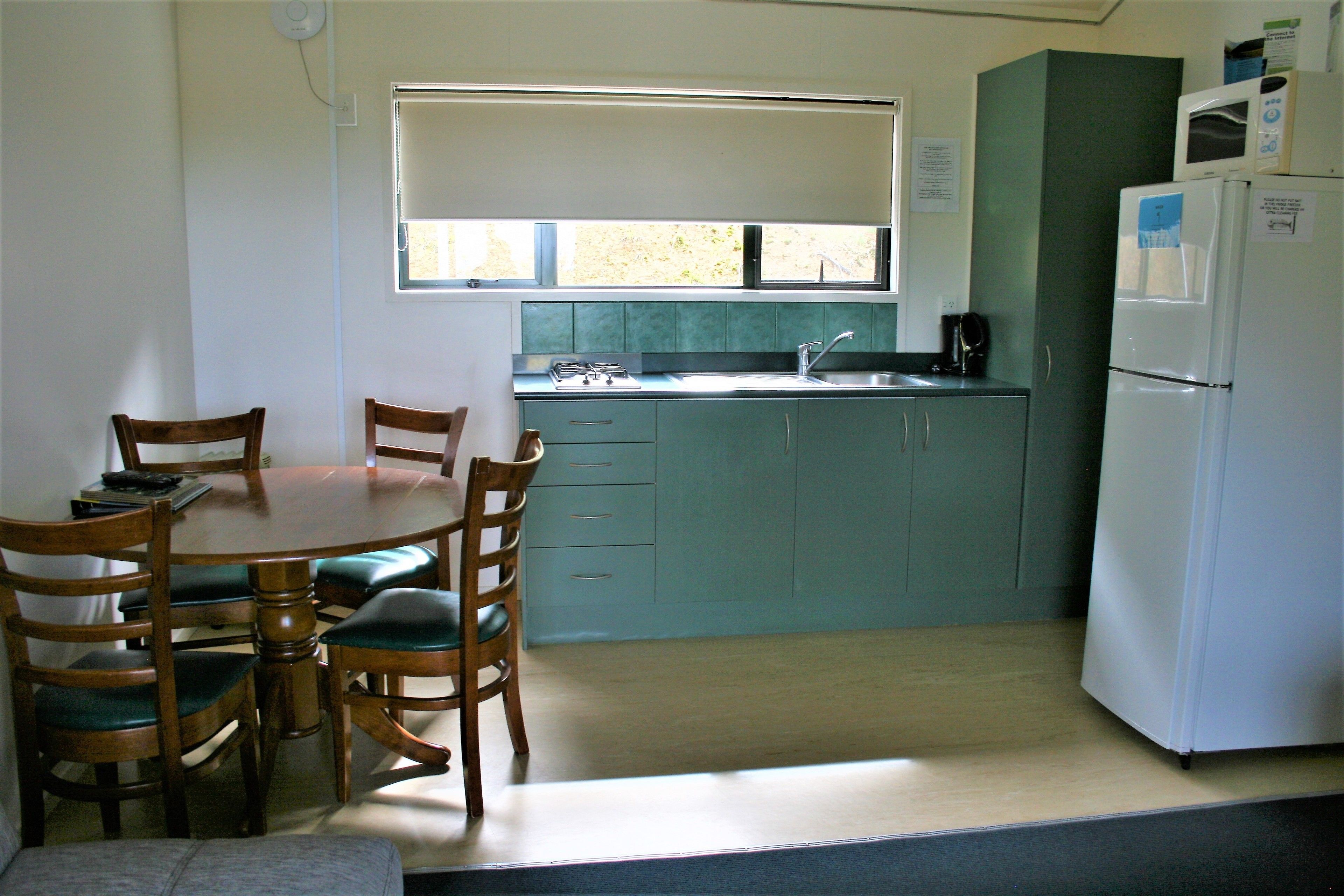 A compact kitchen with a dining table, chairs, a refrigerator, and a window.