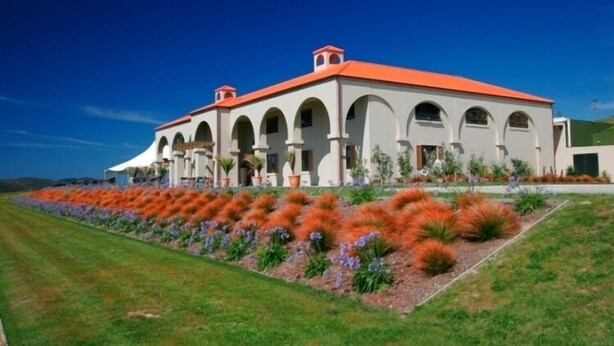 A large, modern building with a red roof and multiple arches. It features a well-maintained lawn with colorful plants in the foreground. - Whatuwhiwhi TOP 10 Holiday Park (Karkari Peninsula)