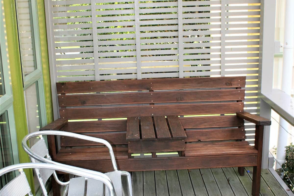 Un banc en bois et deux chaises en métal sont placés sur une terrasse en bois, avec une clôture blanche en arrière-plan.