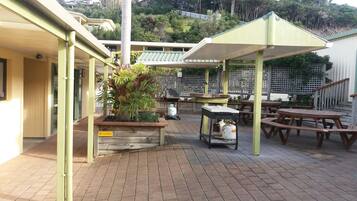 A covered outdoor patio with wooden tables and benches, a barbecue grill, and a gas cylinder.