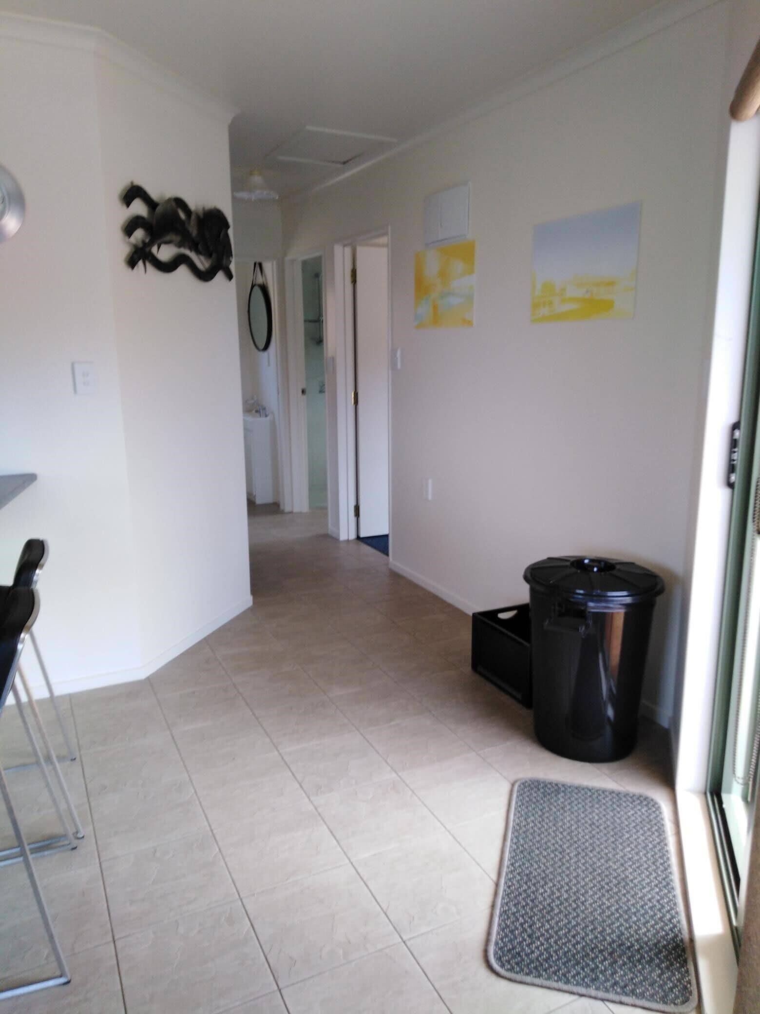 A hallway with a trash bin, a doormat, and a chair.