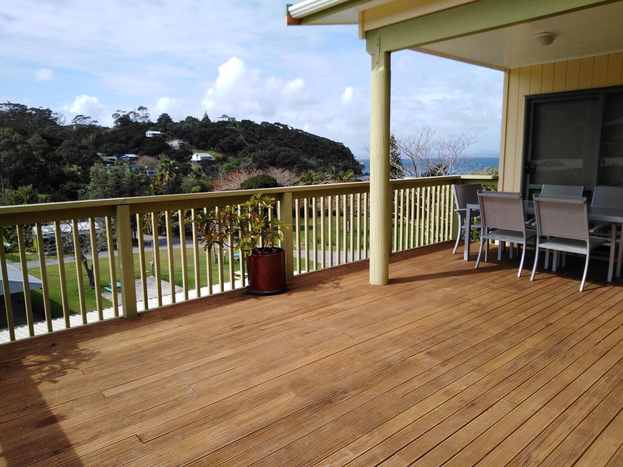 Una terraza de madera con barandilla, una mesa con sillas y una planta en maceta.