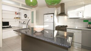 A modern kitchen with a granite countertop, stainless steel appliances, and green pendant lights. - Wattle Holiday Rental (Hawthorn)