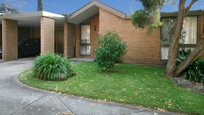 A two-story brick house with a covered garage, a small front yard with grass and shrubs, and a tree. - Wattle Holiday Rental (Hawthorn)