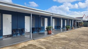 A motel with individual rooms, each with a door and a window. There are outdoor chairs and potted plants near the entrance. - Innisfail City Motel (Innisfail)