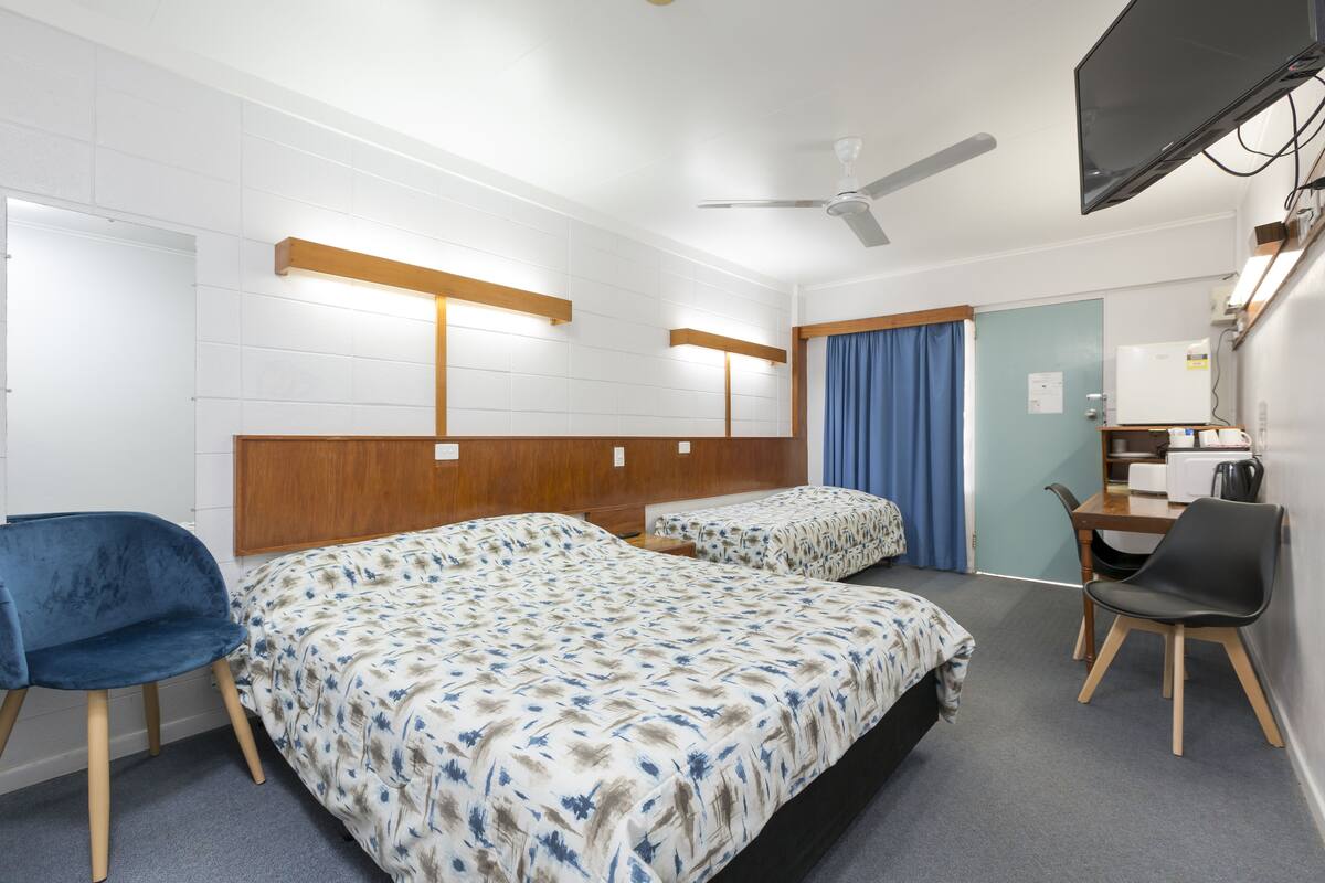 A hotel room with two beds, a desk, a chair, a television, and a ceiling fan.