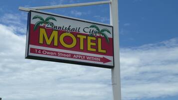 Une enseigne de motel ornée de motifs de palmiers et portant l’inscription : « Danisfail City MOTEL, 14, rue Owen. Les candidatures sont reçues sur place. »
