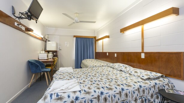 A hotel room with a bed, a desk with a computer, a chair, and a ceiling fan. - Innisfail City Motel (Innisfail)