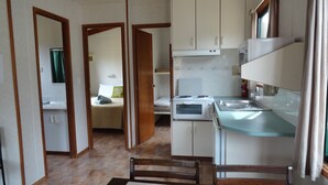 A compact kitchen with a stove, microwave, and sink, adjacent to a bedroom with a bed and a window. - Kangaroo Island Cabins (Kingscote)