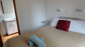 A hotel room with a bed, a bedside table, a small shelf, a mirror, and a wardrobe.