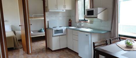 A compact kitchen with a stove, microwave, and sink. There is a small dining area with a table and chairs.