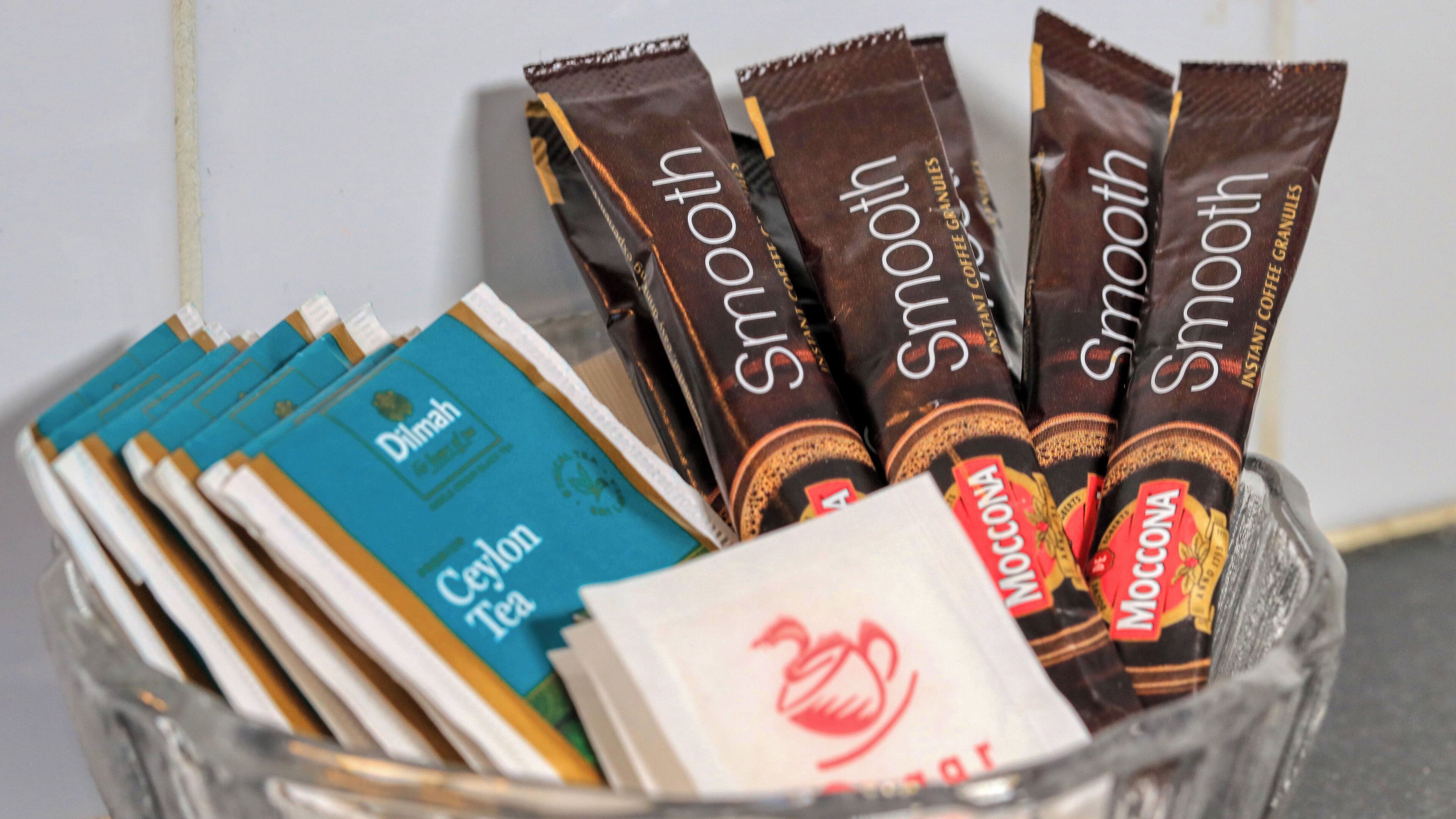 Un récipient en verre contenant des sachets de café instantané et des sachets de thé.