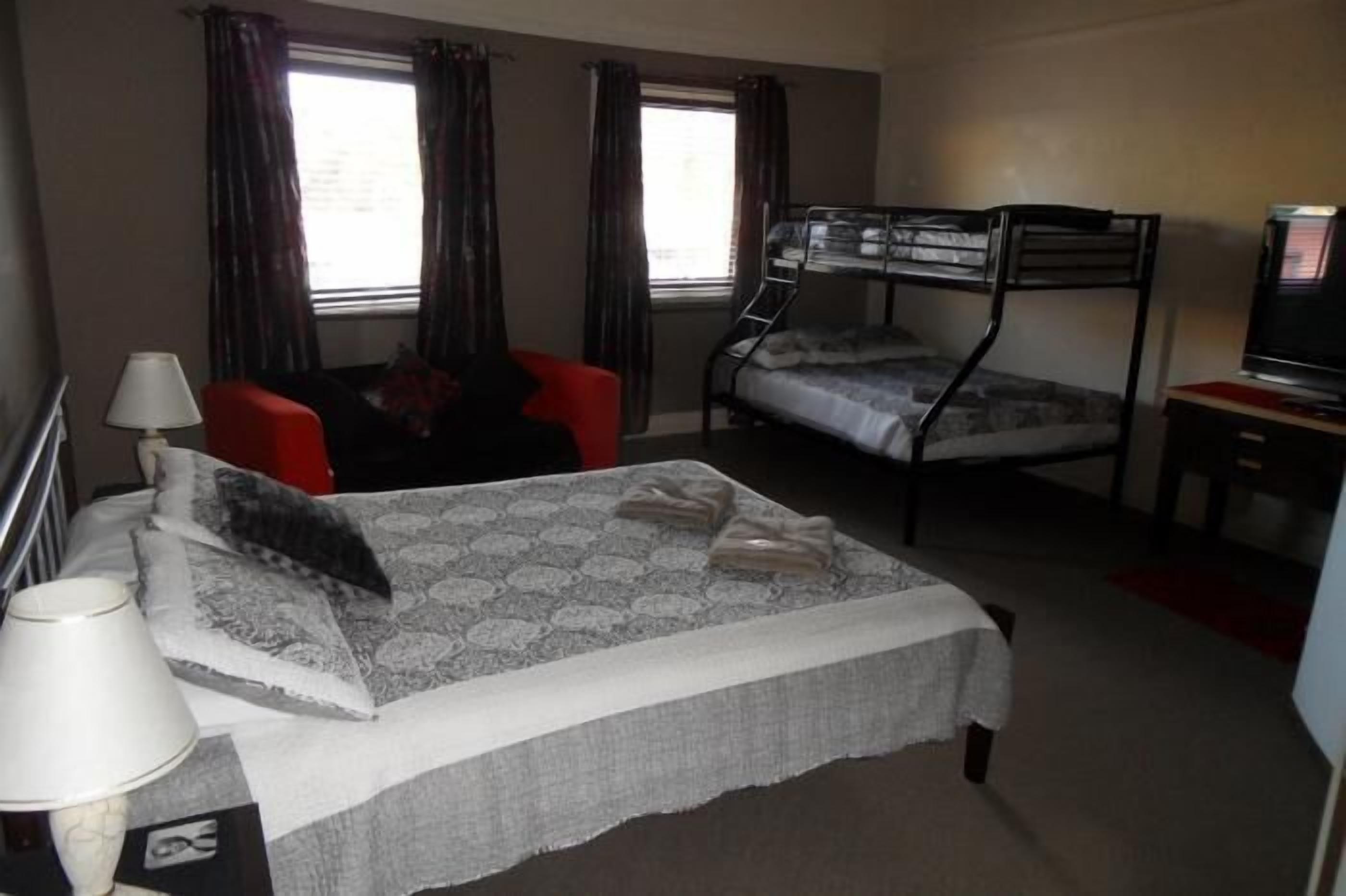 A hotel room with bunk beds, a desk with a television, a chair, and a lamp.