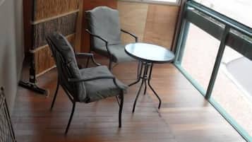 Una habitación con piso de madera, dos sillas grises, una pequeña mesa redonda y un ventanal con vistas a la calle.