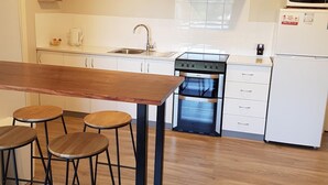 A modern kitchen with a wooden bar table, four stools, a stainless steel range hood, a built-in oven, and a white refrigerator.