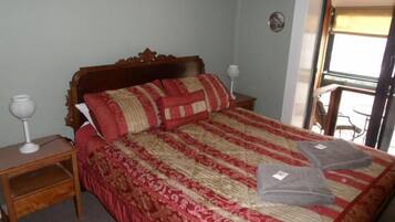 Una cama bien hecha con una colcha estampada, dos almohadas y una mesita de noche con una lámpara.