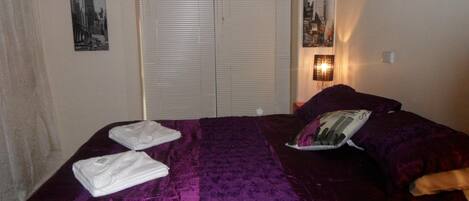 A hotel room with a bed, a door with blinds, and a wall-mounted lamp.
