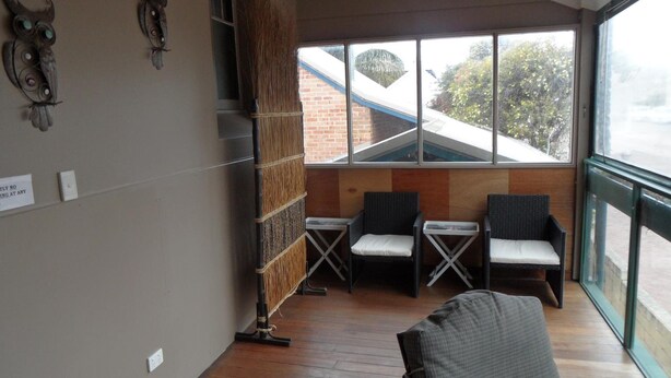 A room with a large window, two wicker chairs, a wooden floor, and decorative wall art.