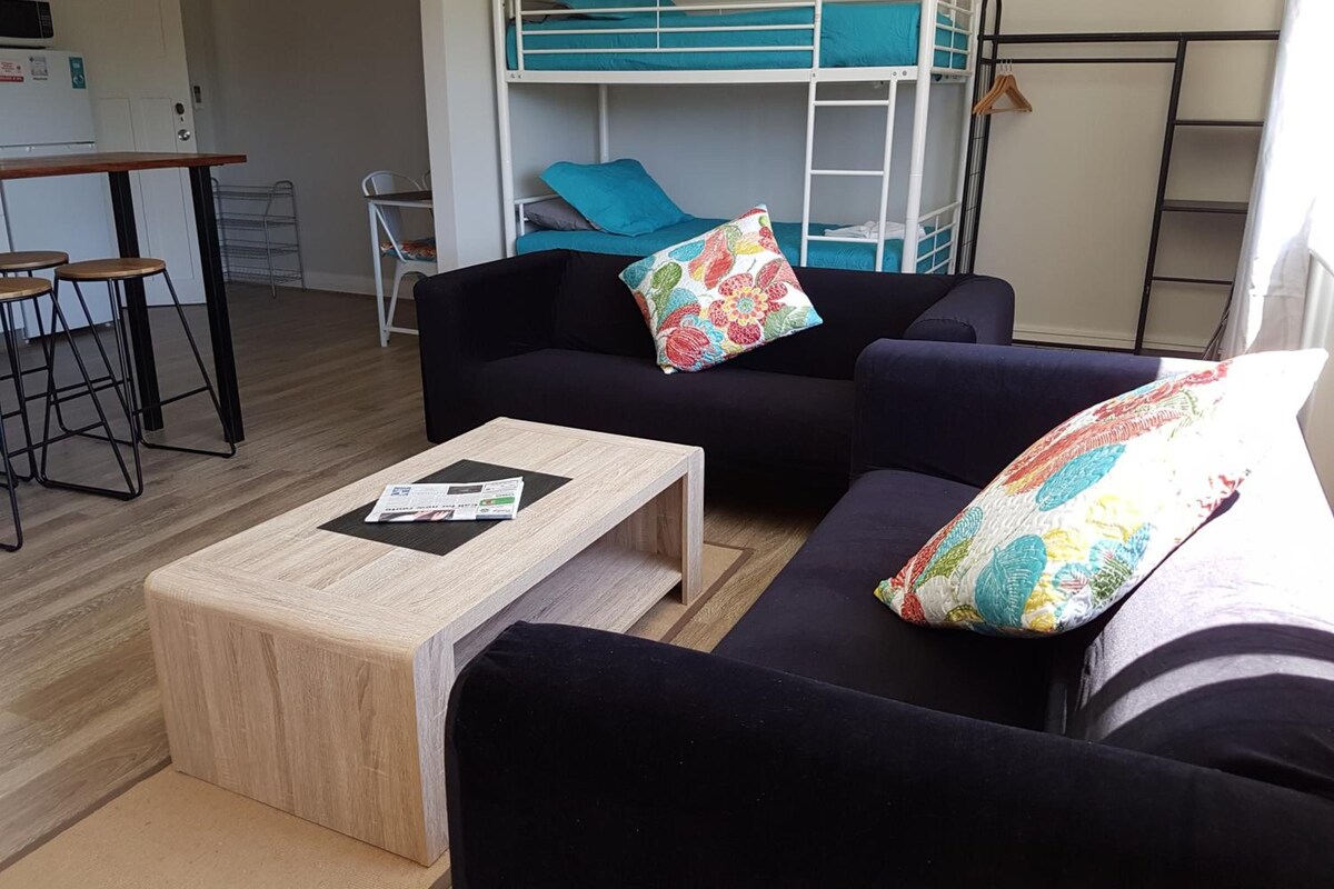 Une chambre meublée comprenant un canapé, une petite table, un lit superposé et un coin cuisine.