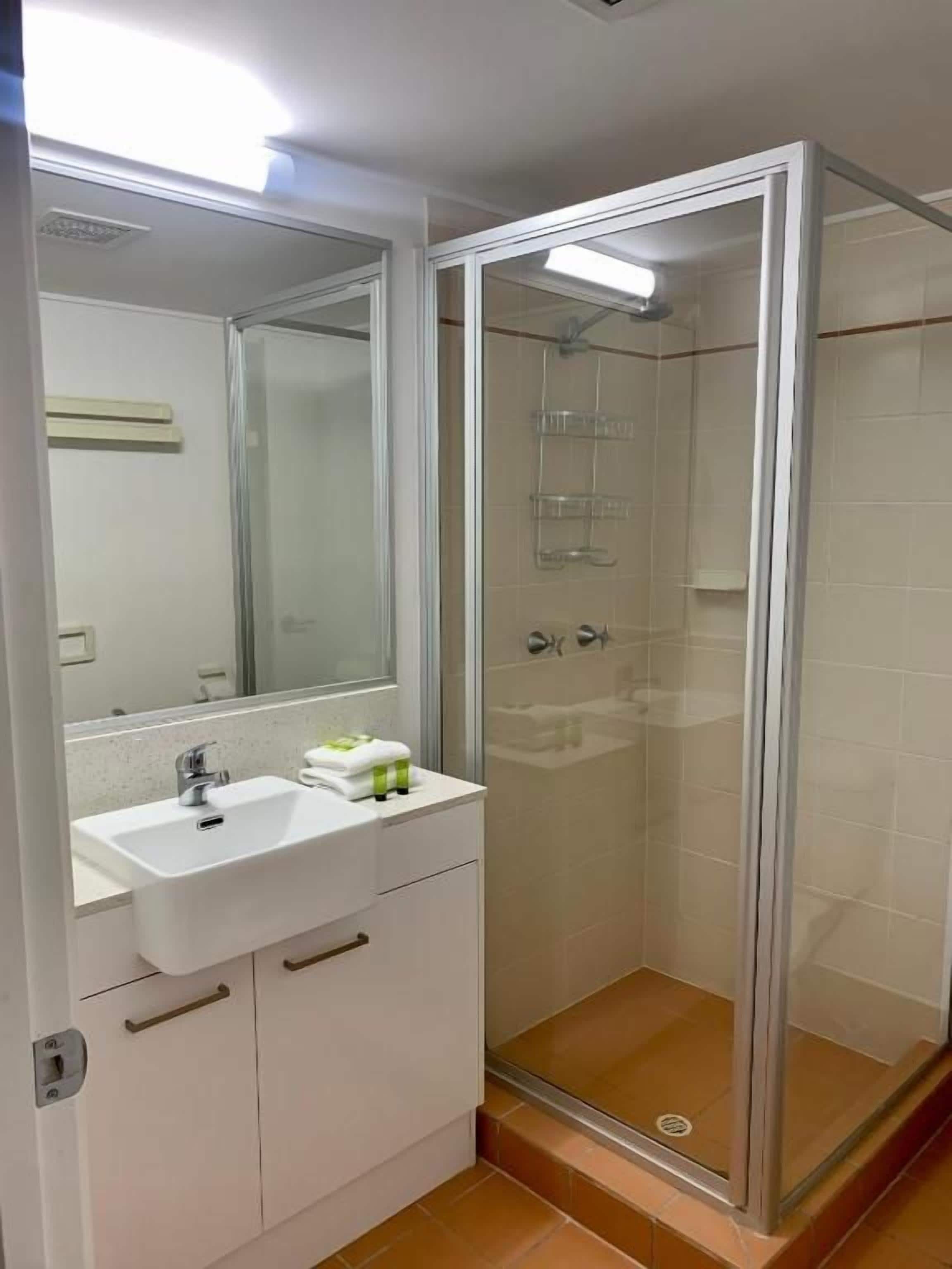 A bathroom with a glass-enclosed shower, a white sink with a mirror above it, and a cabinet below.