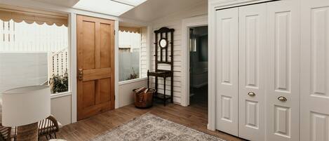 A room with a wooden door, a white wardrobe, a patterned rug, wicker furniture, and a window with a view of a fence.