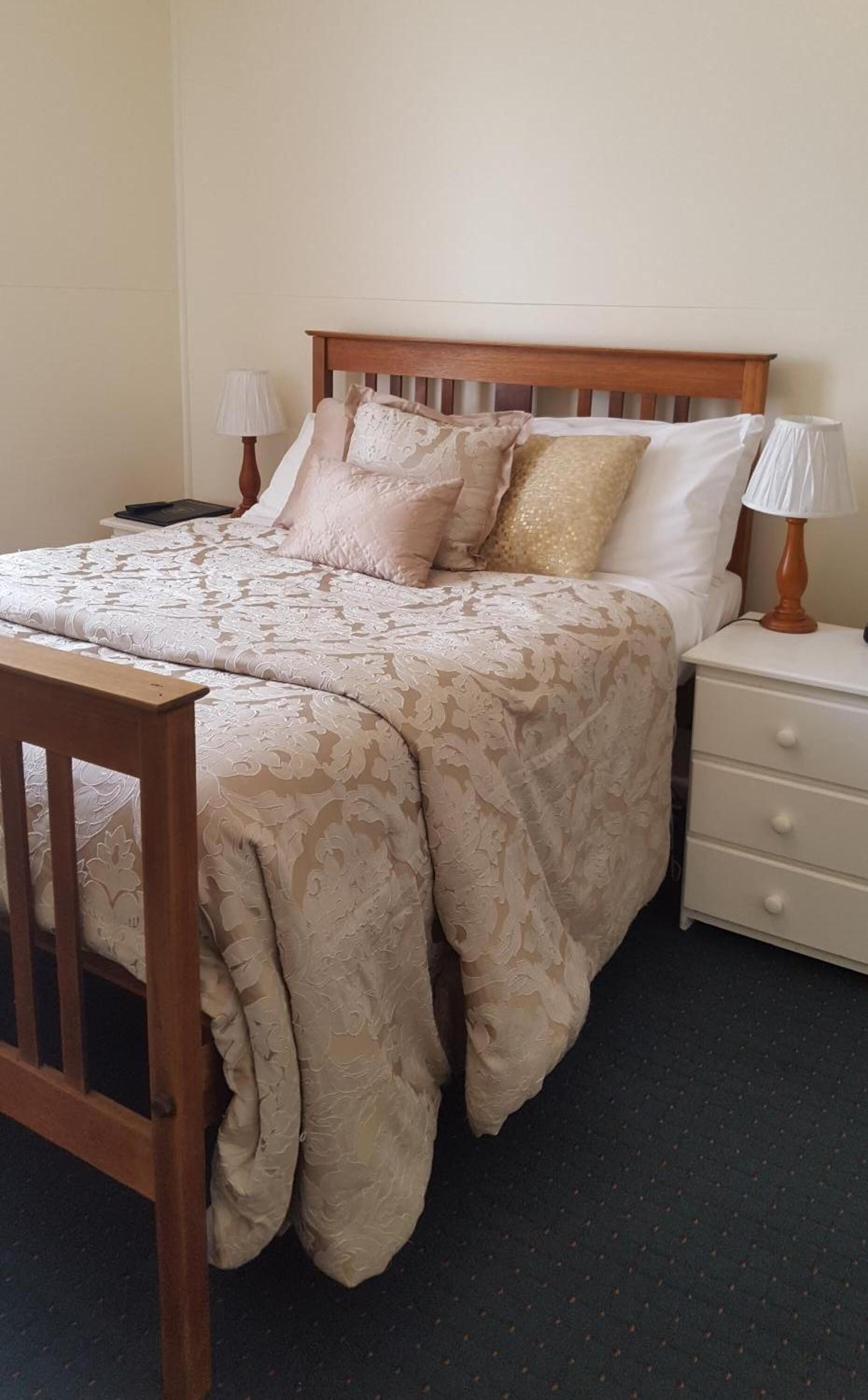 A neatly made bed with a patterned bedspread, a wooden headboard, and two bedside lamps.