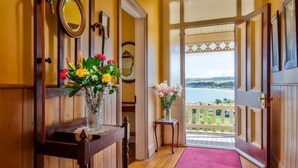 Un pasillo con paneles de madera, un espejo y un florero con flores. Se ve una puerta que da a un balcón con vista al agua.