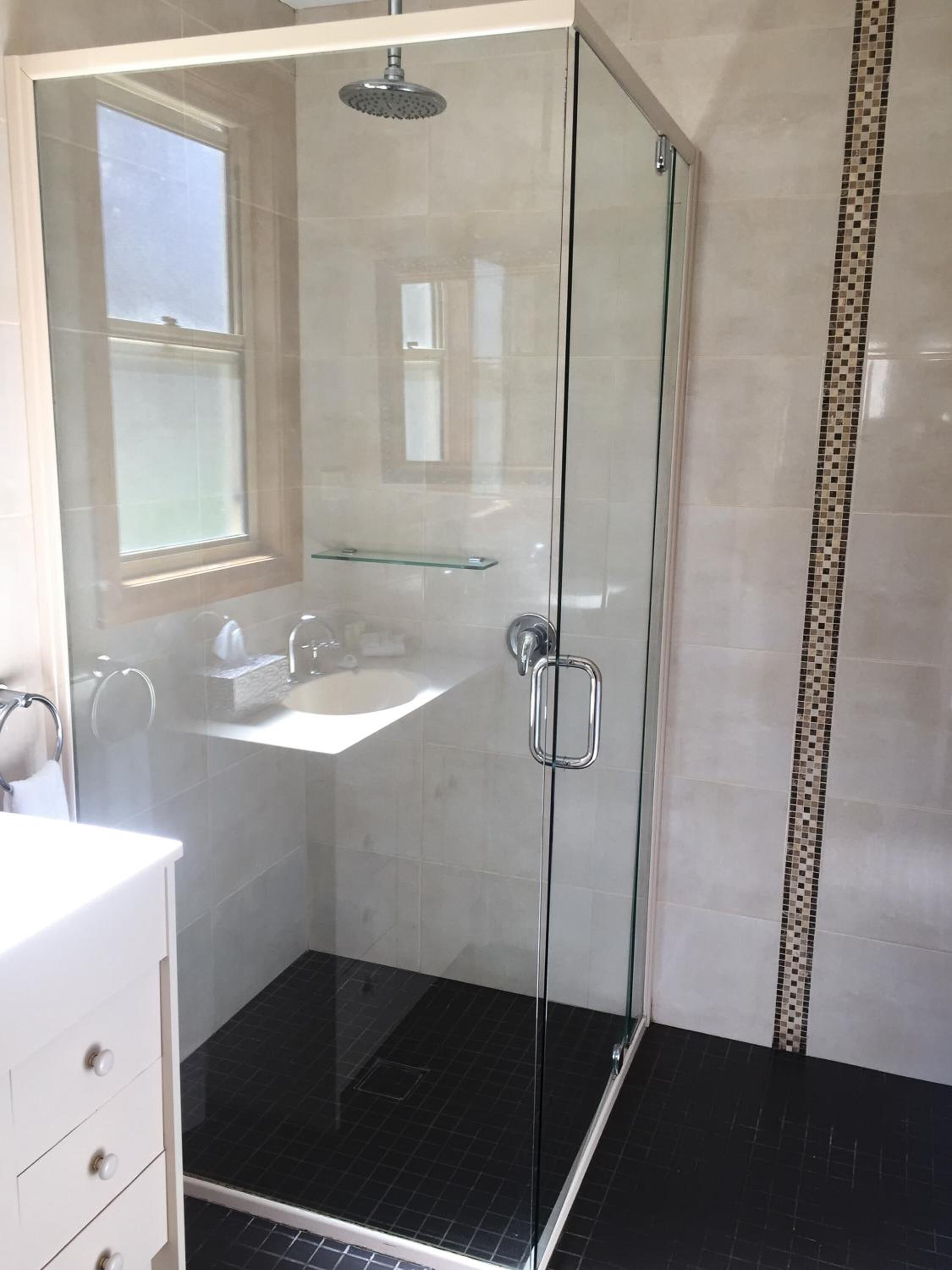 A glass-enclosed shower with a handheld showerhead, a glass shelf, and a white sink with a mirror.