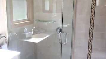 A glass-enclosed shower with a handheld showerhead, a glass shelf, and a white sink with a mirror.