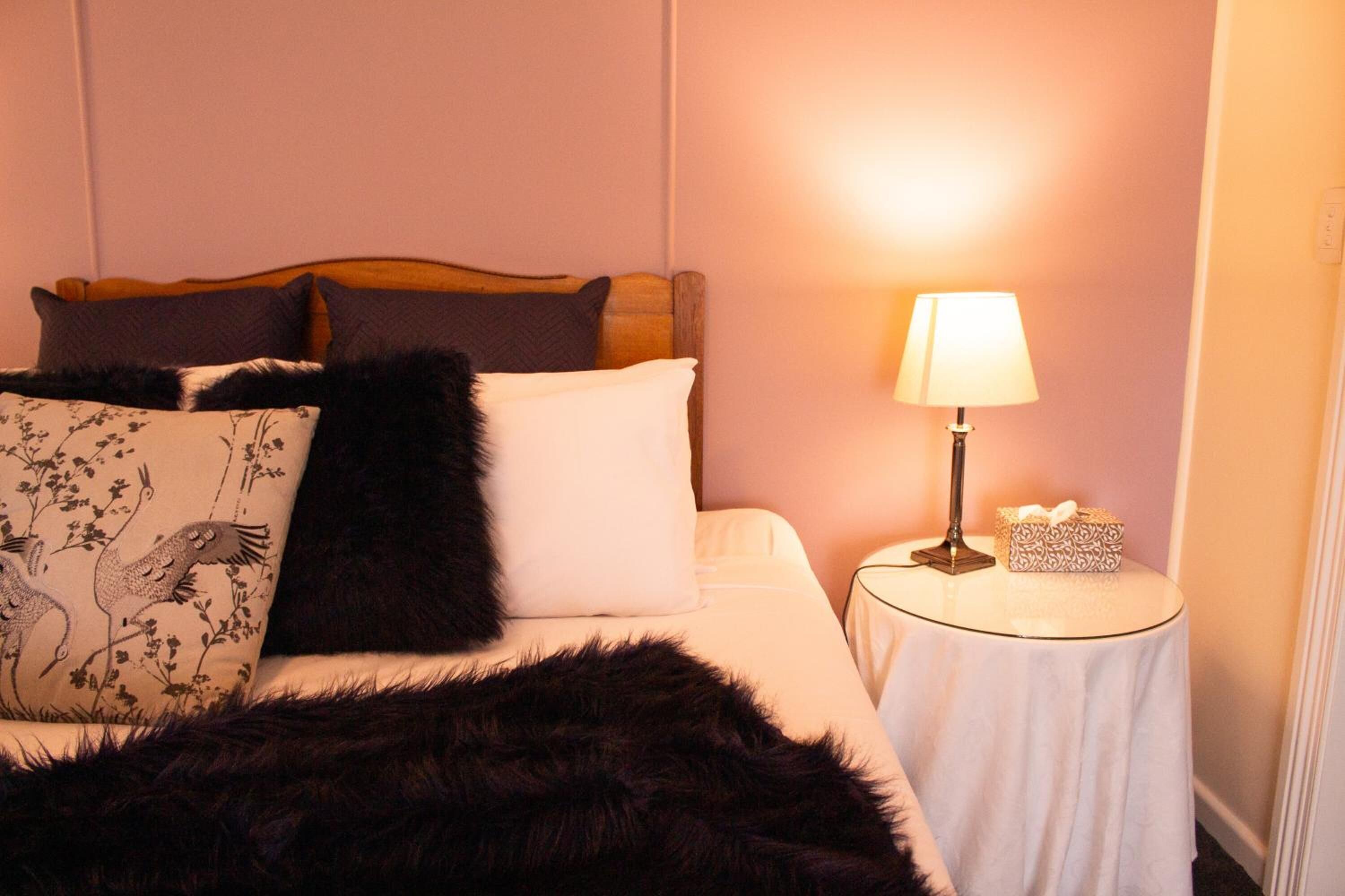 A neatly made bed with a black fur throw, a lamp on a bedside table, and a floral pillow.