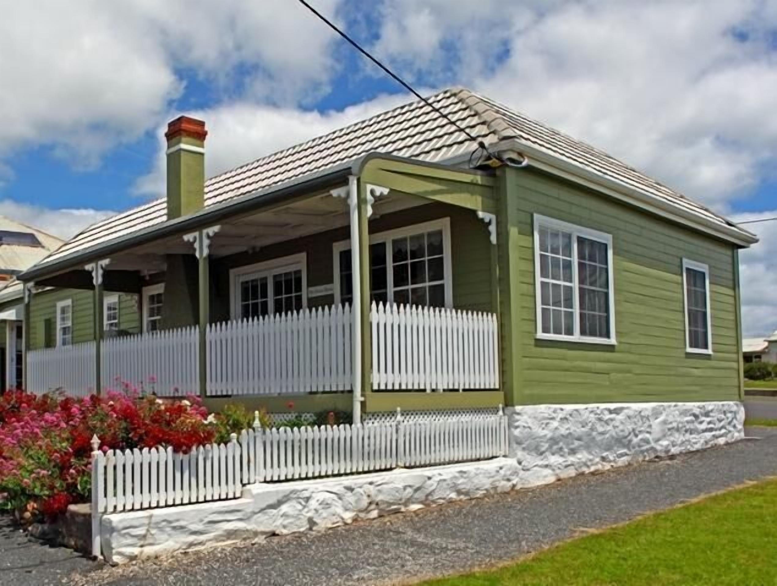 A single-story house with a porch, white picket fence, and a stone foundation.