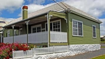 A single-story house with a porch, white picket fence, and a stone foundation.