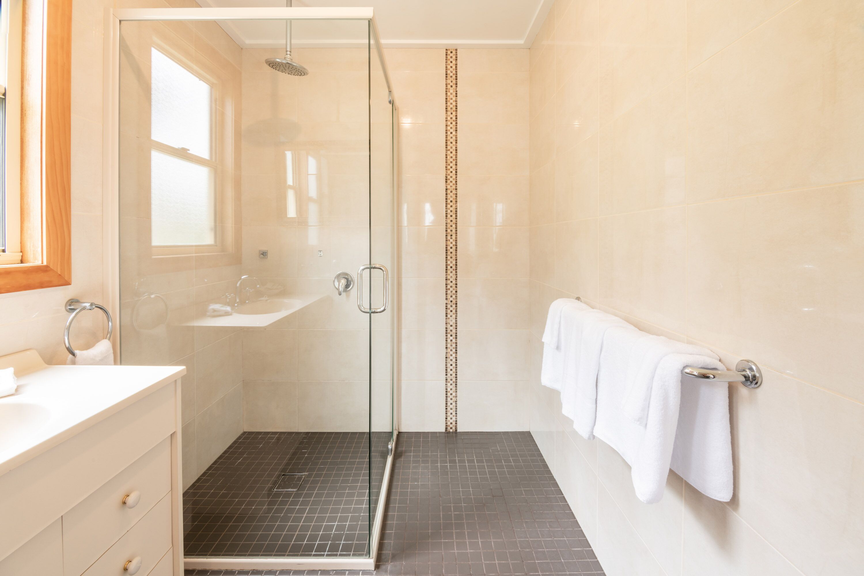 A modern bathroom with a glass-enclosed shower, a white sink, and a towel rack.