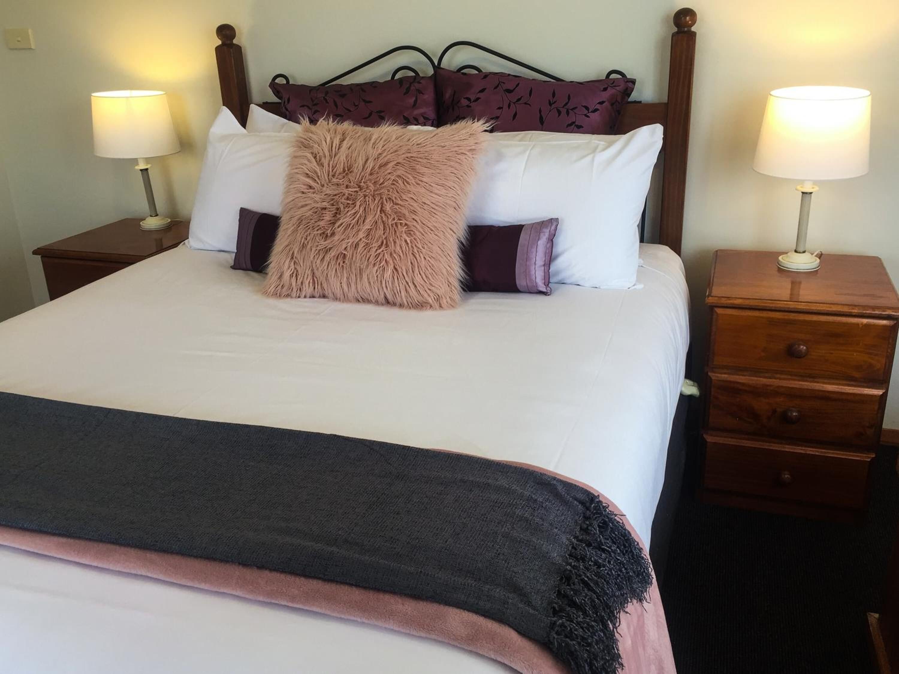 A neatly made bed with a fluffy pillow, two bedside tables with lamps, and a wooden nightstand with drawers.