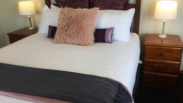 A neatly made bed with a fluffy pillow, two bedside tables with lamps, and a wooden nightstand with drawers.