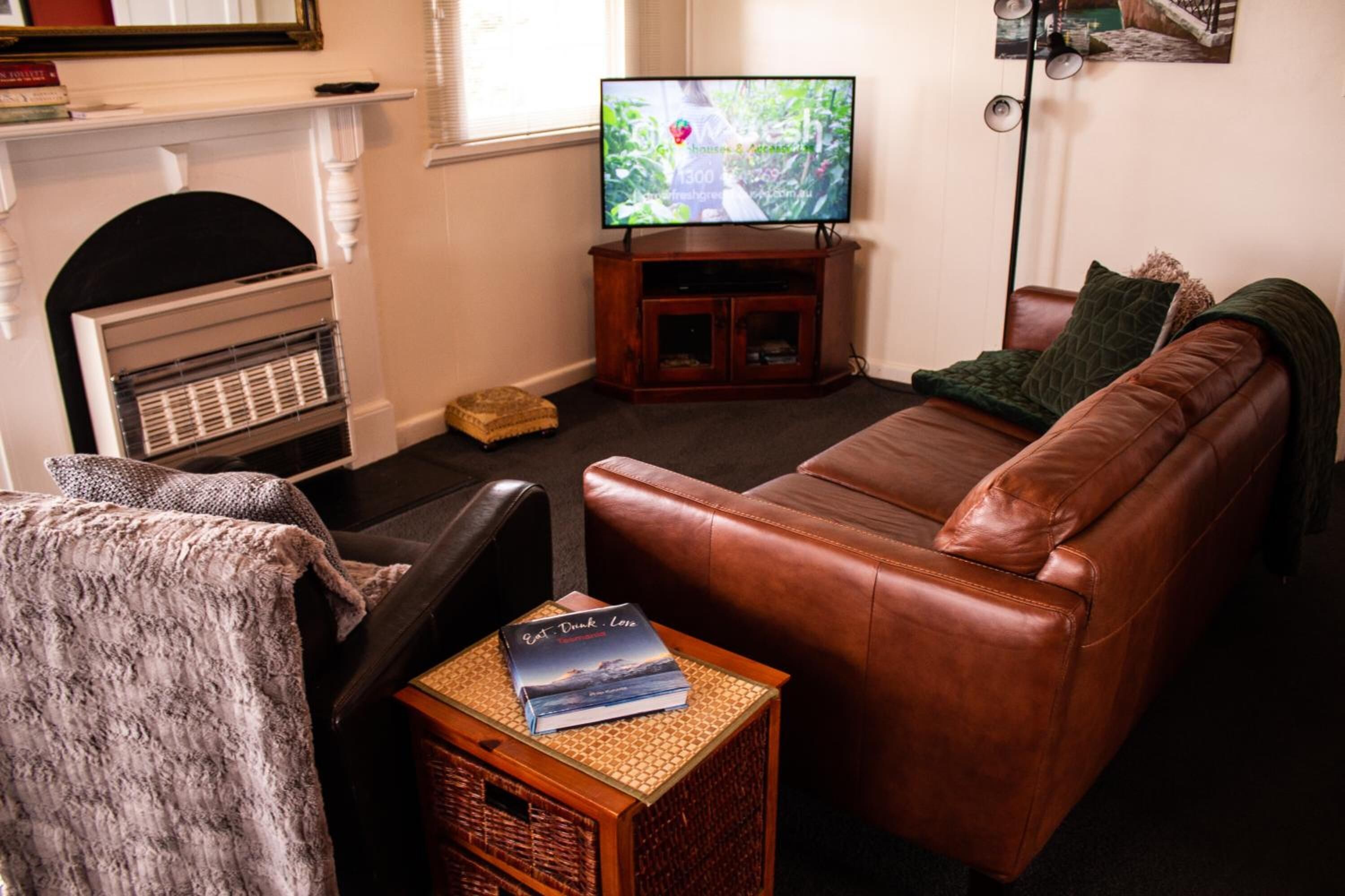 A living room with a leather sofa, a television on a wooden stand, a fireplace, and a bookshelf.