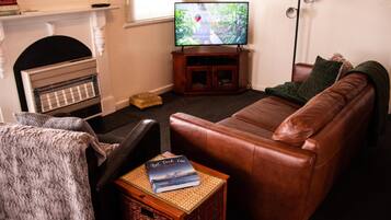 A living room with a leather sofa, a television on a wooden stand, a fireplace, and a bookshelf.