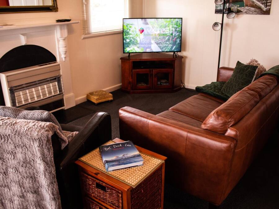 A living room with a leather sofa, a television on a wooden stand, a fireplace, and a bookshelf.