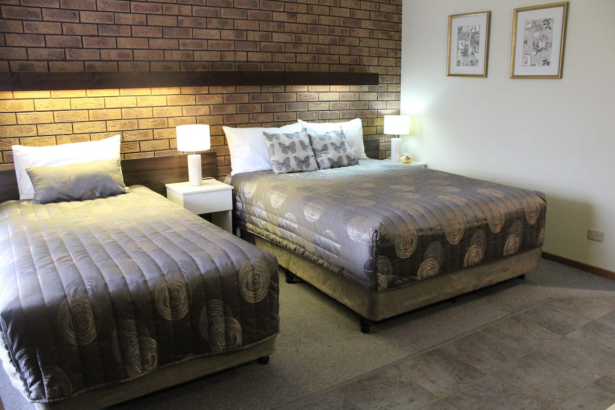 A double bed with a patterned bedspread and two pillows, a nightstand with a lamp, and a brick-patterned headboard.
