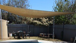 A swimming pool with a curved edge, surrounded by a shaded area and a fenced backyard. - Dunolly Golden Triangle Motel (Dunolly)