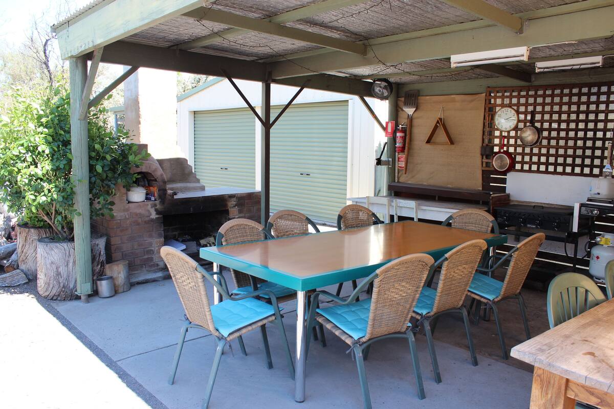 An outdoor patio with a long table and chairs, a brick fireplace, and a grill.